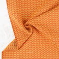 A close-up of textured fabric with a repeating orange and beige chevron pattern, draped to show its soft texture and folds.