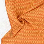 A close-up of textured fabric with a repeating orange and beige chevron pattern, draped to show its soft texture and folds.