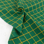 Green fabric with a yellow grid pattern, draped and folded to show its texture and weave.