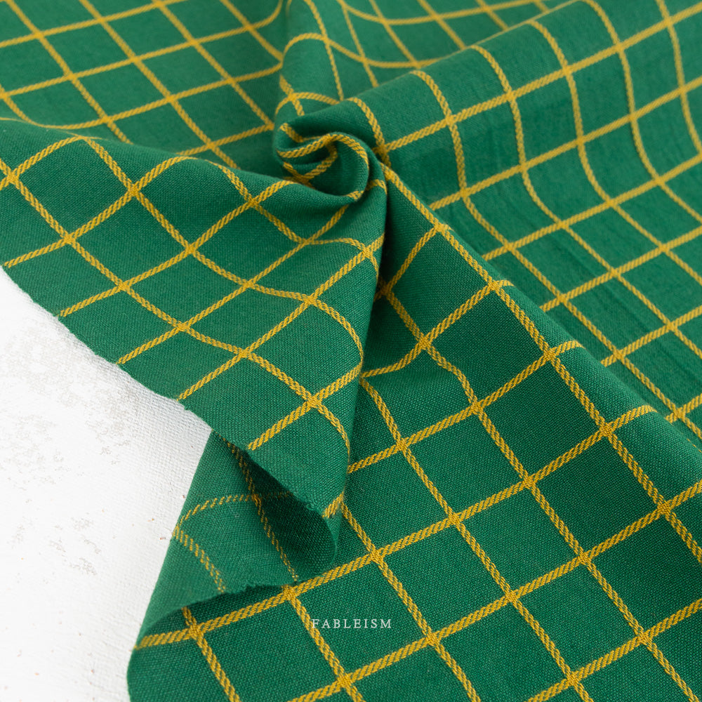 Green fabric with a yellow grid pattern, draped and folded to show its texture and weave.