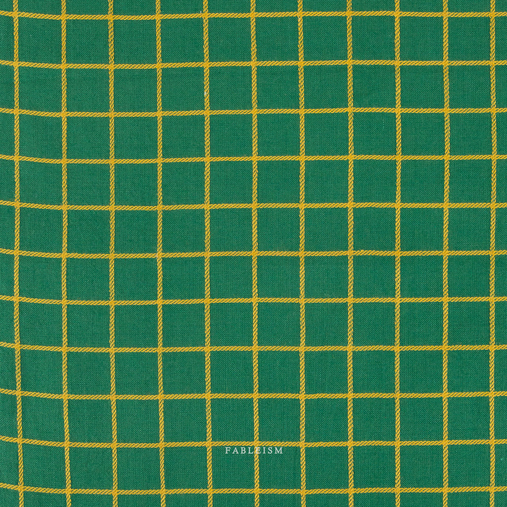 A close-up of green fabric with a yellow grid pattern, showing the woven texture and a small 'FABLEISM' watermark near the bottom center.