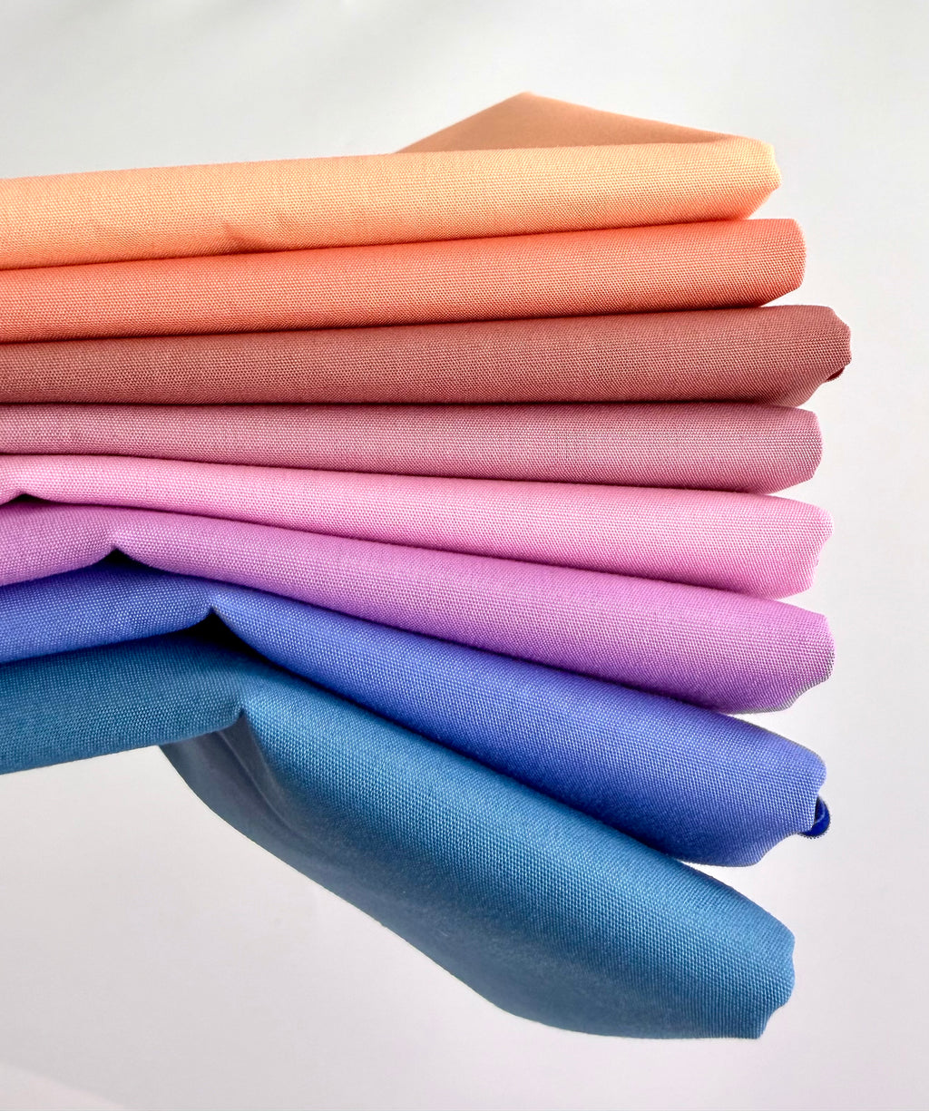 Stack of colorful fabric swatches in various shades on a white background