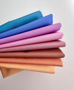 Stack of colorful fabric swatches in blue, purple, pink, brown, and beige on a light gray background.