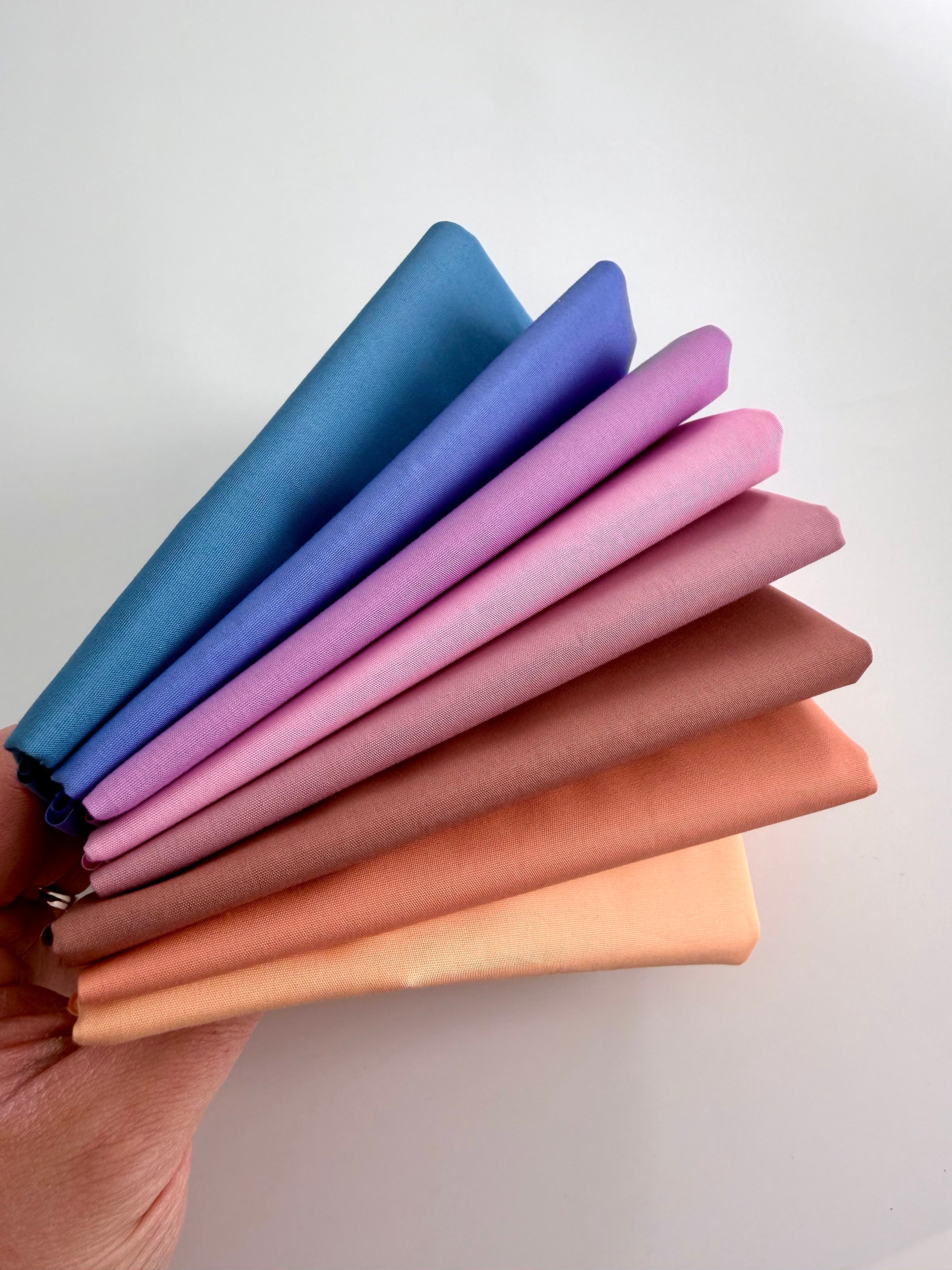 Stack of colorful fabric swatches held by a hand on a light background