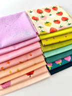 A bright, overhead shot of sixteen overlapping folded fabric pieces. Features a gradient of lavender, bubblegum pink, and peach fabrics with star and strawberry prints, a large-scale strawberry print on cream, transitioning into zesty lime greens, mint, and deep teal fabrics with pink strawberry motifs. The entire collection is displayed against a clean white background.