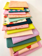 A bright, overhead shot of sixteen overlapping folded fabric pieces. Features a gradient of lavender, bubblegum pink, and peach fabrics with star and strawberry prints, a large-scale strawberry print on cream, transitioning into zesty lime greens, mint, and deep teal fabrics with pink strawberry motifs. The entire collection is displayed against a clean white background.