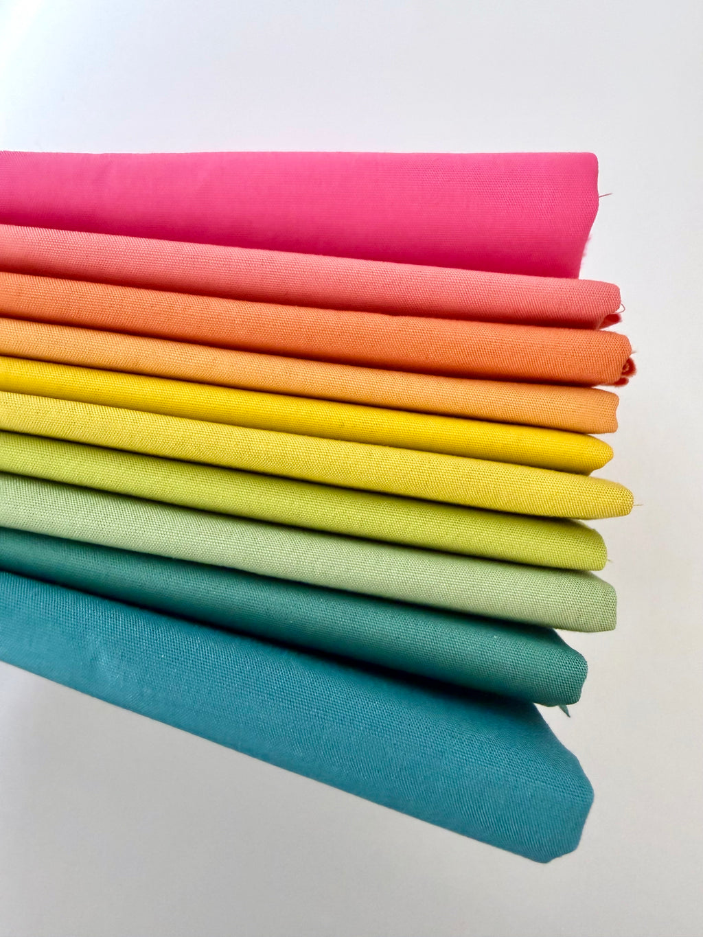 Stack of colorful fabric swatches in a gradient from pink to blue on a white background