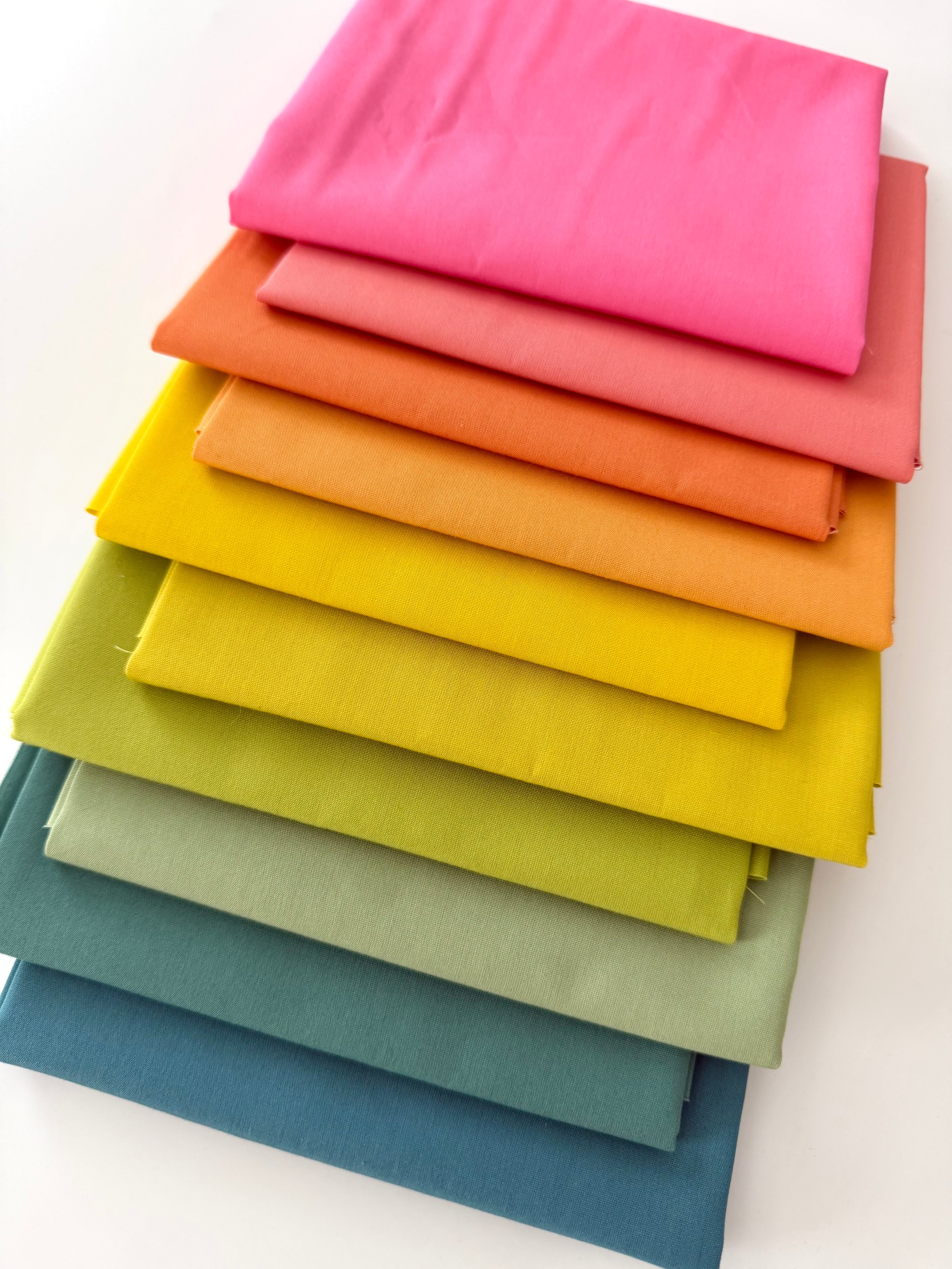 Stack of colorful fabric swatches in various shades on a white background