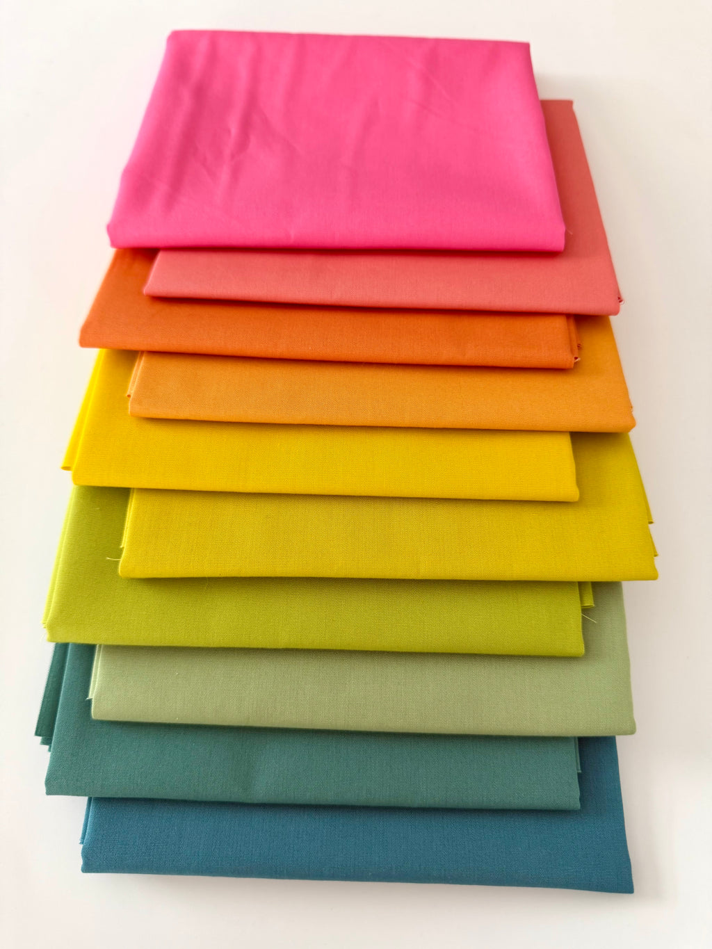 Stack of colorful fabric swatches in various shades on a white background
