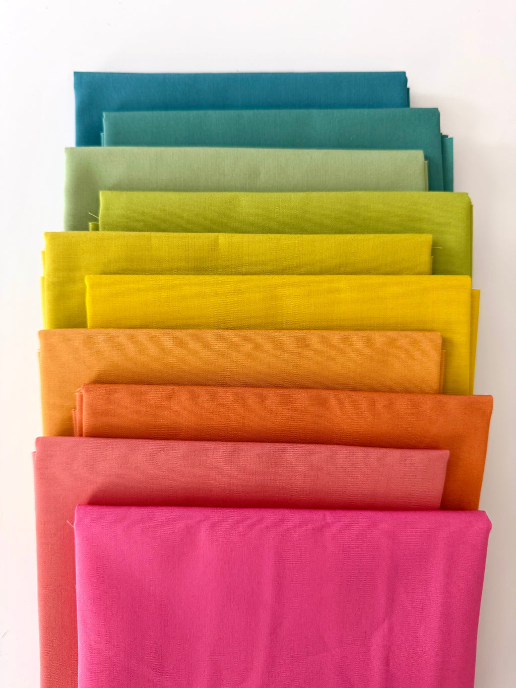 Stack of colorful fabric swatches in various shades on a white background