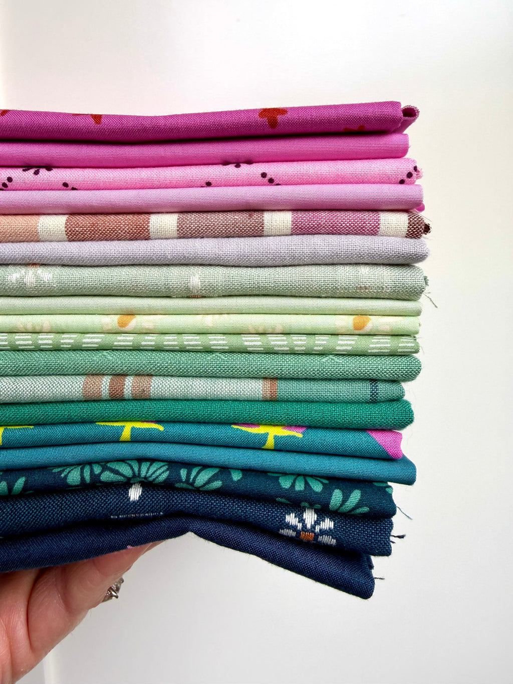Stack of colorful fabric swatches held by a hand against a white background