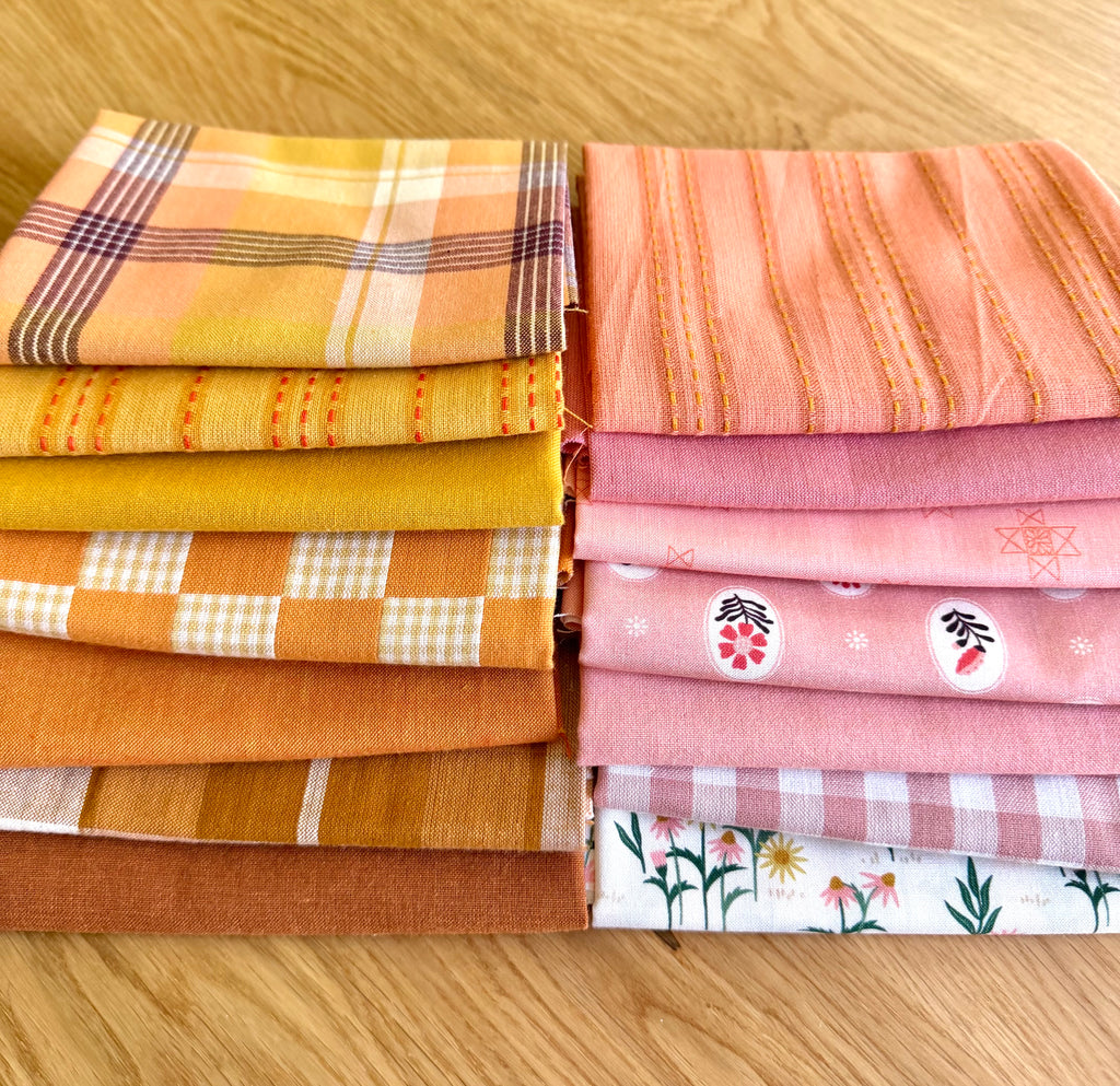 A curated stack of 14 high-quality fabric quarters from the Golden Hour Glow bundle. The mix features rich mustard yellow, deep terracotta rust, soft blush pink, cream, and warm neutral fabrics. The collection showcases a blend of textures and patterns, including yarn-dyed wovens, classic ginghams, windowpane plaids, delicate stripes, and a central floral botanical print, styled flat on a wooden surface.