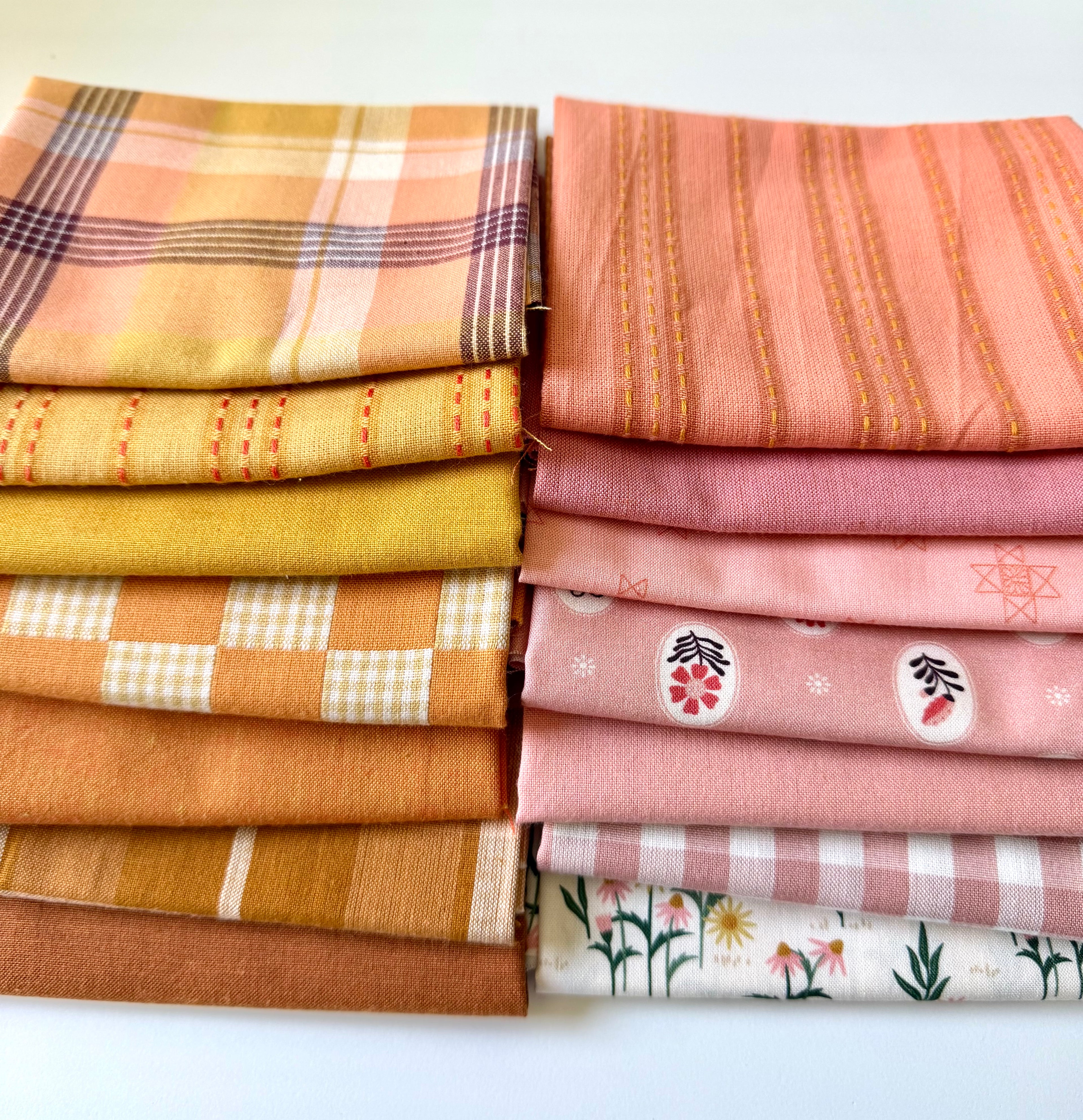 A curated stack of 14 high-quality fabric quarters from the Golden Hour Glow bundle. The mix features rich mustard yellow, deep terracotta rust, soft blush pink, cream, and warm neutral fabrics. The collection showcases a blend of textures and patterns, including yarn-dyed wovens, classic ginghams, windowpane plaids, delicate stripes, and a central floral botanical print, styled flat on a clean white background.
