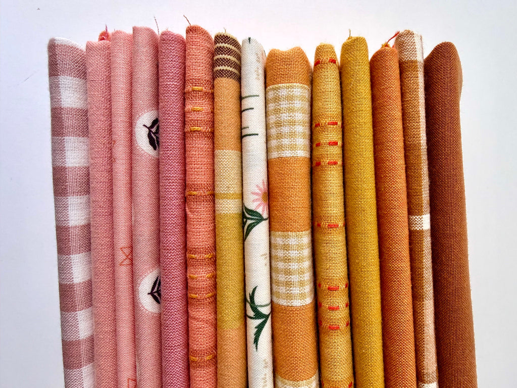 A curated stack of 14 high-quality fabric quarters from the Golden Hour Glow bundle. The mix features rich mustard yellow, deep terracotta rust, soft blush pink, cream, and warm neutral fabrics. The collection showcases a blend of textures and patterns, including yarn-dyed wovens, classic ginghams, windowpane plaids, delicate stripes, and a central floral botanical print, styled flat on a clean white background.