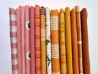 A curated stack of 14 high-quality fabric quarters from the Golden Hour Glow bundle. The mix features rich mustard yellow, deep terracotta rust, soft blush pink, cream, and warm neutral fabrics. The collection showcases a blend of textures and patterns, including yarn-dyed wovens, classic ginghams, windowpane plaids, delicate stripes, and a central floral botanical print, styled flat on a clean white background.
