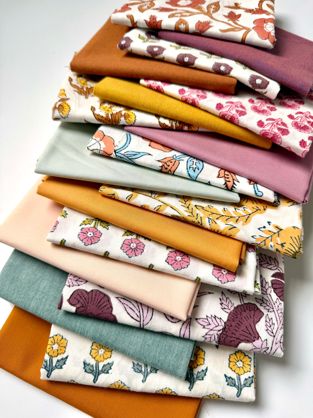 Stack of colorful fabric swatches with floral patterns on a white background