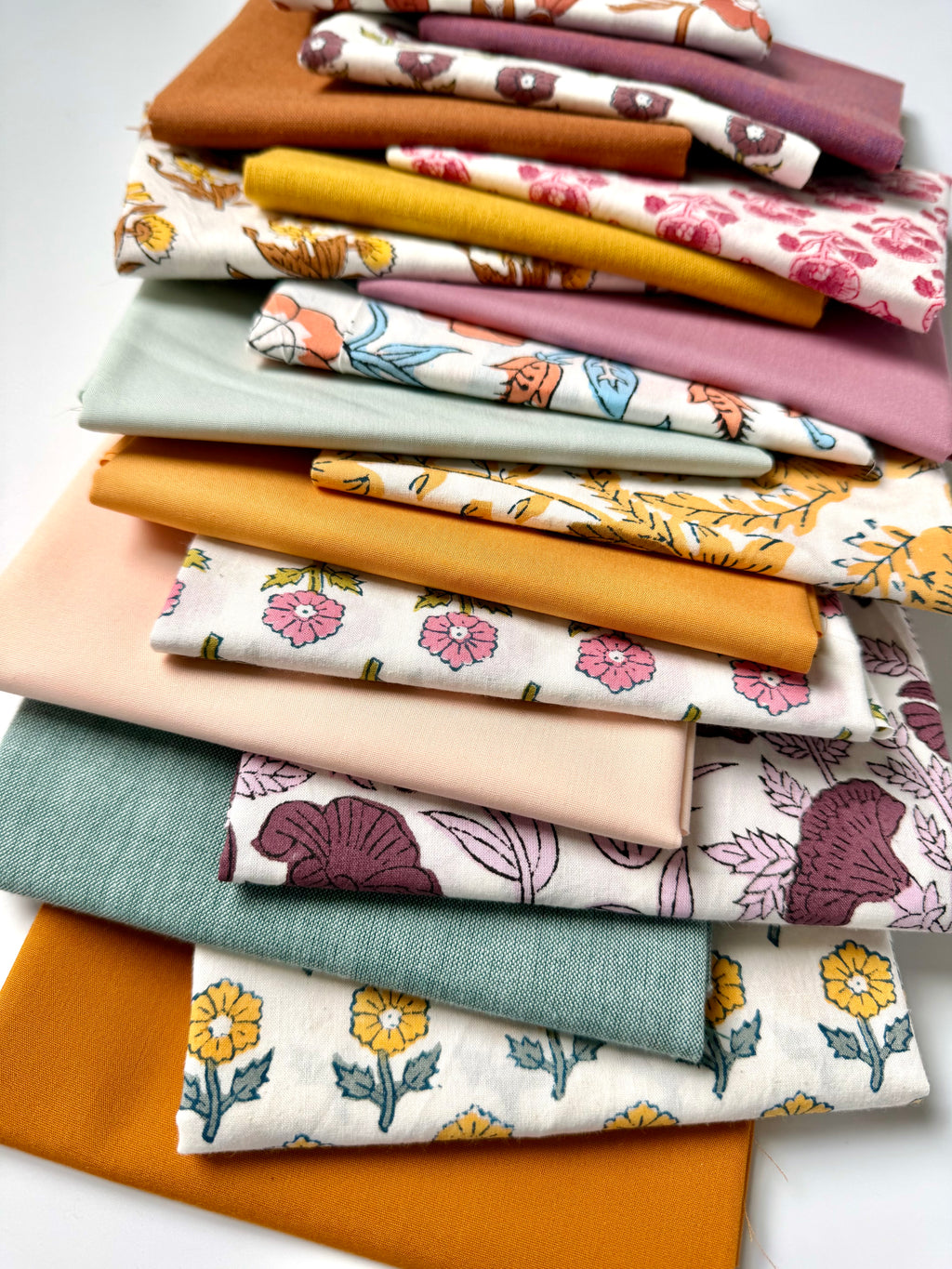 Stack of colorful fabric swatches with floral and solid patterns on a white background