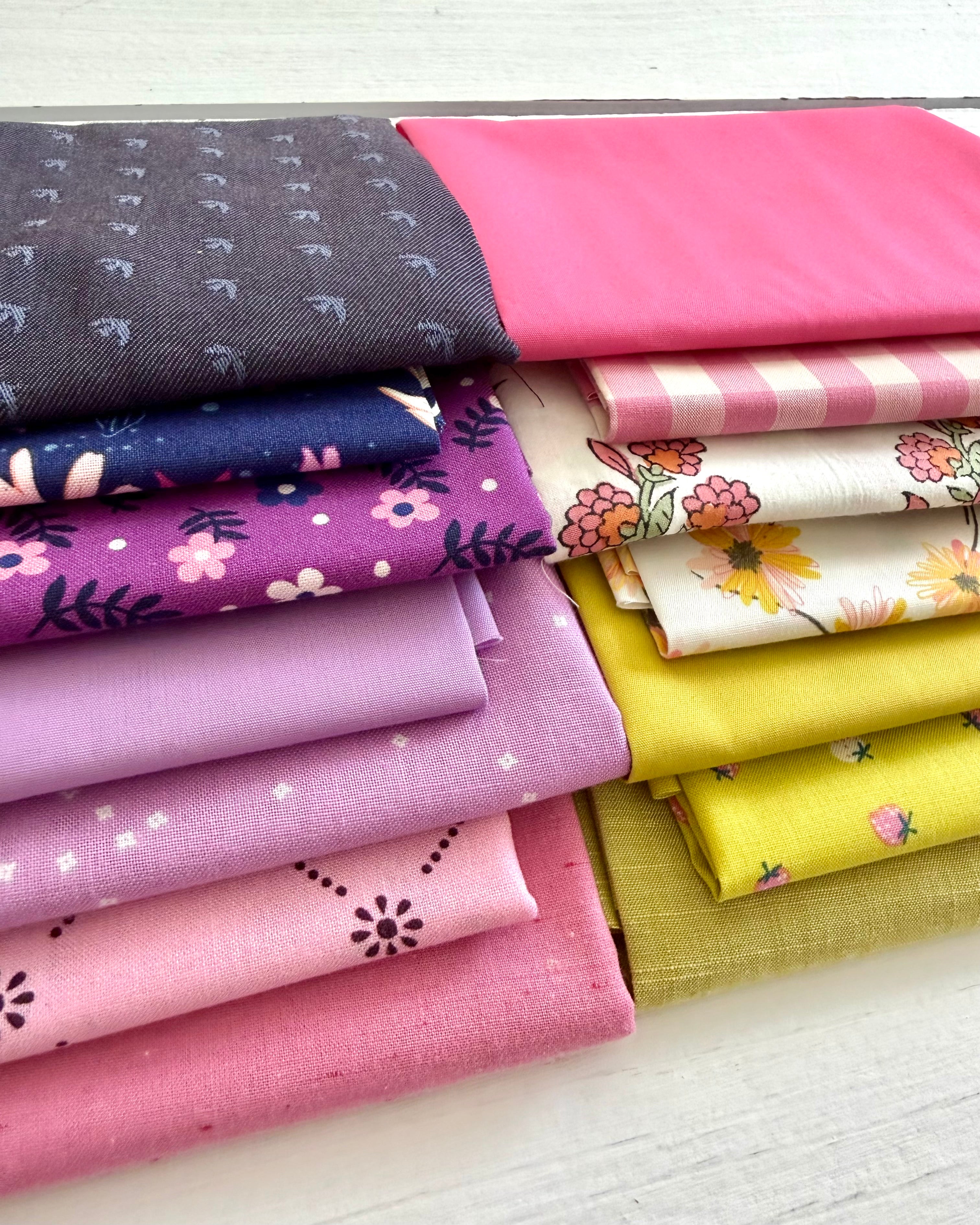 Stack of colorful fabric swatches neatly folded on a white wooden surface