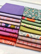 Two stacks of folded fabric samples in assorted colors and patterns, including solid purple, floral green, pink, orange, red, and plaid designs, arranged on a white wood surface.