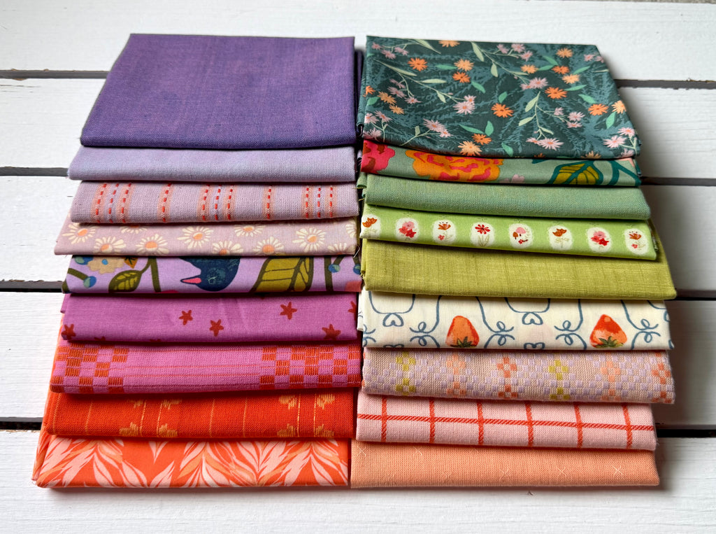 Two stacks of folded fabric samples with various patterns and colors, including purple, green floral, orange, pink, and red, arranged on a white wooden background.