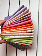 A hand holds a fanned-out stack of colorful patterned fabric swatches against a white wooden plank background.