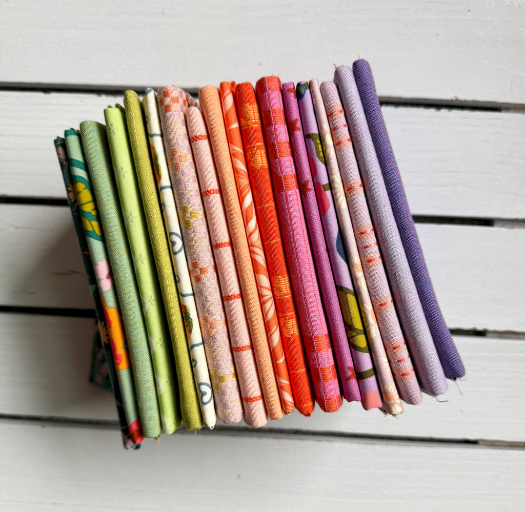 A stack of folded patterned fabric swatches in various colors and designs, arranged vertically on a white painted wooden surface.