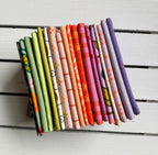 A stack of folded patterned fabric swatches in various colors and designs, arranged vertically on a white painted wooden surface.