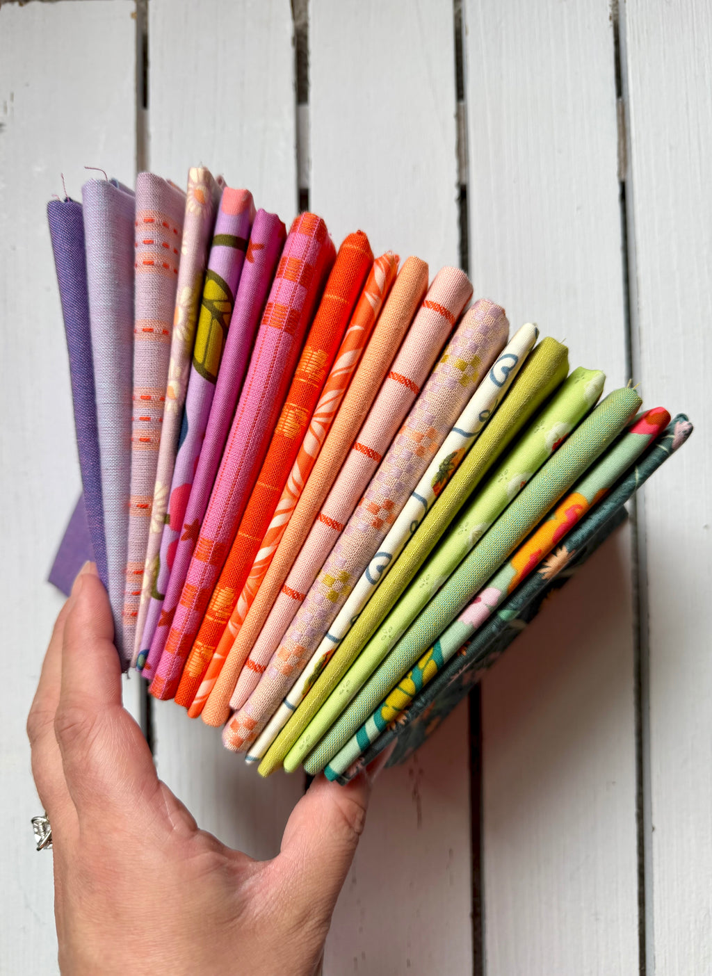 A hand holds a fanned-out selection of colorful patterned fabric swatches against a white wooden plank background.