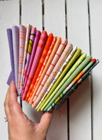 A hand holds a fanned-out selection of colorful patterned fabric swatches against a white wooden plank background.