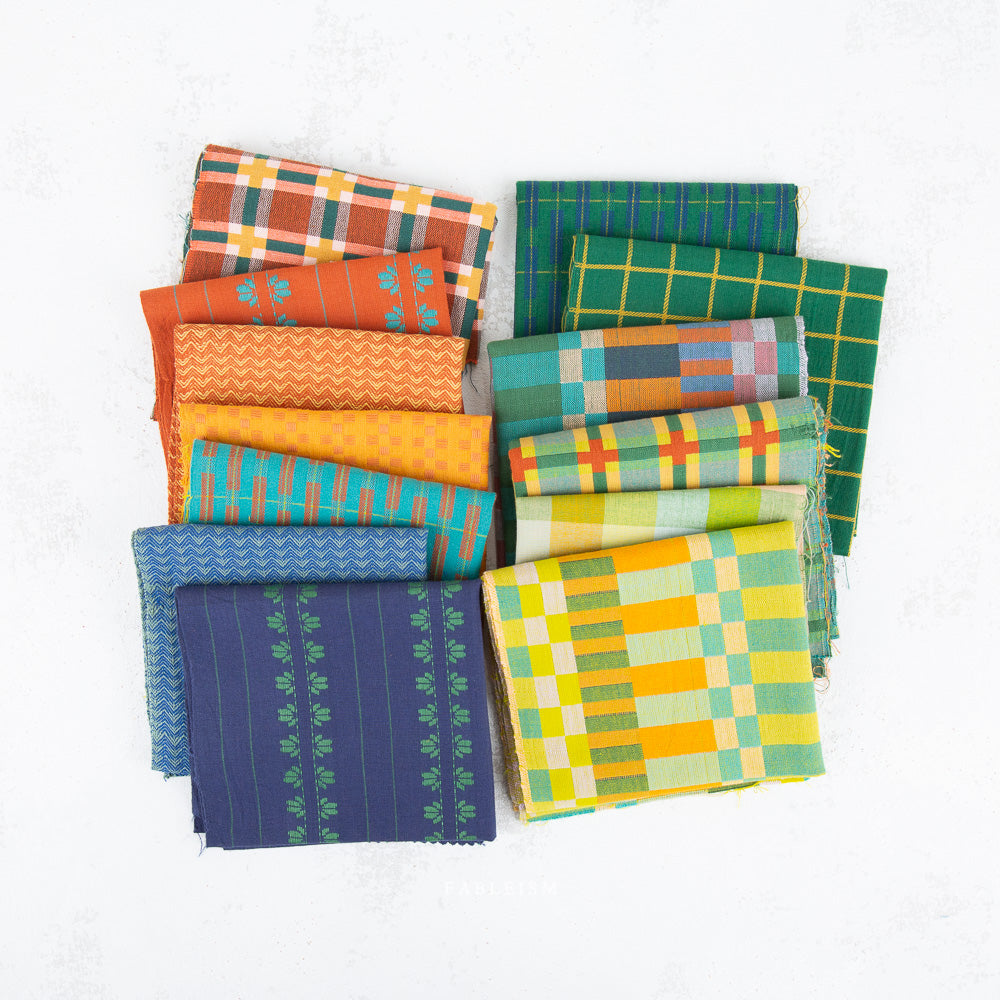 A collection of folded patterned fabric pieces in multiple colors and designs, including plaid, stripes, and chevrons, arranged on a light textured background.