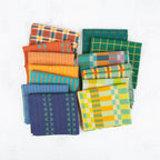A collection of folded patterned fabric pieces in multiple colors and designs, including plaid, stripes, and chevrons, arranged on a light textured background.